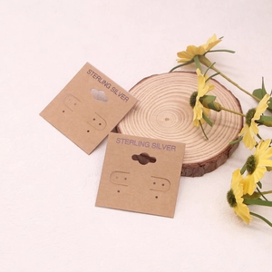 Detail view of square kraft paper earring display cards with pre-cut holes on a wooden base