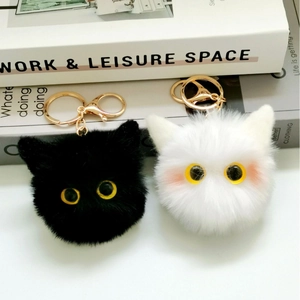Close-up of black and white plush cat ball keychains with large yellow eyes and gold clasp