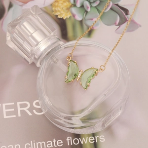 Detailed shot of green butterfly pendant with gold chain on glass perfume bottle