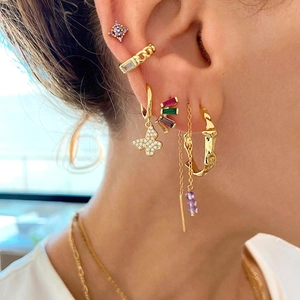 Detailed view of gold butterfly earrings and purple zircon studs worn in a stacked style