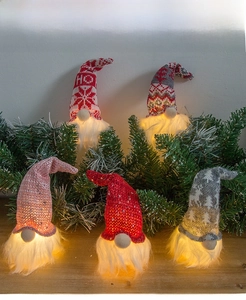 Close-up of five illuminated Christmas gnome ornaments with knitted hats on pine branches