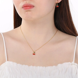 Close-up of model wearing cherry pendant necklace and earrings with red enamel and gold finish
