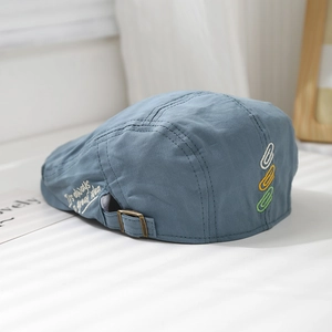 Detail of blue cotton beret featuring side embroidery and bronze metal adjustable buckle