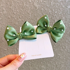 Detailed view of handmade green ribbon bow hair clips with white pearls for girls