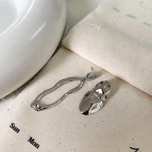 Macro shot of asymmetrical silver geometric earrings on a minimalist linen background