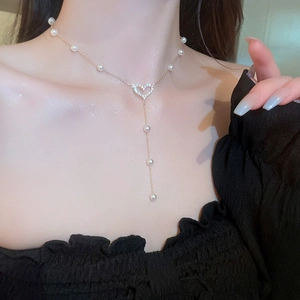 Detailed view of gold heart necklace with white pearls and sparkling tassel elements