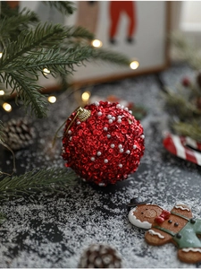 Detail of red Christmas ball with sparkling sequins and white beads on a pine tree