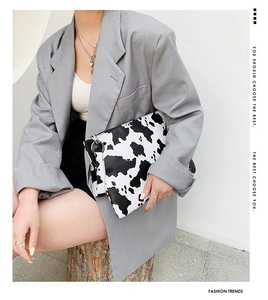 Cow print clutch bag featured in a street style look with grey blazer and wrist strap