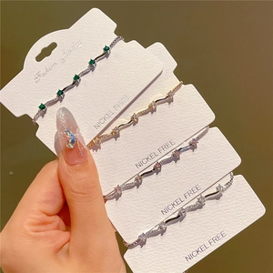 Hand holding four sparkling zircon bracelets in emerald, gold, pink and clear colors