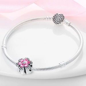 Detalle macro de pulsera de serpiente plateada con flor de esmalte rosa y dijes de pavé