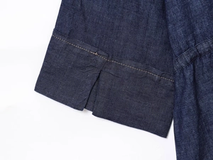 Vista macro del tessuto denim blu scuro con cuciture a contrasto e dettaglio spacco laterale