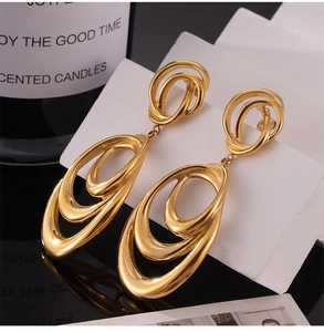 Macro detail of triple-layered oval gold drop earrings on a white stand with reflections