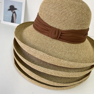 Close-up of four stacked khaki straw sun hats with elegant brown decorative ribbons