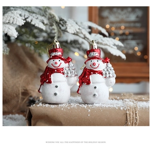 Close-up of festive snowman ornaments with red hats holding silver trees on snowy branches