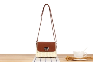 Close-up of woven straw crossbody bag with brown leather flap and silver metal buckle
