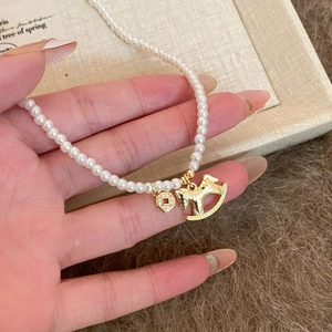 Detailed close-up of zircon pearl necklace with golden horse and coin charms for women