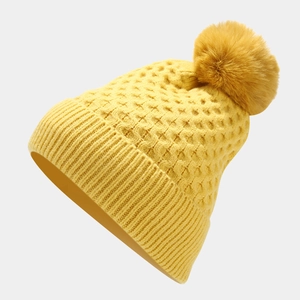 Detailed texture of ginger yellow knitted beanie hat with a fluffy oversized faux fur pompom