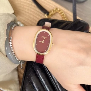 Detail of red leather watch band with golden oval dial and MISHALI branding logo