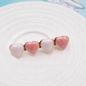 Detail of gold metal hair clip featuring white and pink heart charms on a white plate