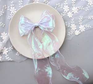 Detail of iridescent pink bow hair clip with wavy silver edges and long flowing ribbons