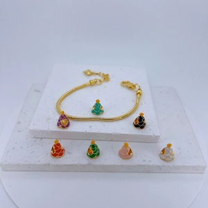 Gold snake chain bracelet with colorful enamel pendants on white stone display