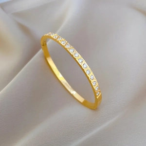 Close-up of a gold stainless steel zircon bracelet on a soft silk fabric background