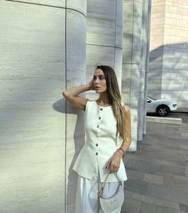 Détail du haut à basque blanc élégant avec boutons dorés et pantalon large assorti
