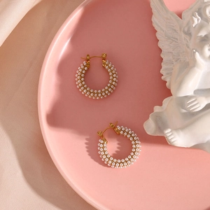 Macro detail of 18K gold plated hoop earrings set with small white pearls on a pink plate