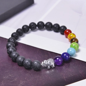 Bracelet chakra en pierre de lave avec breloque éléphant argentée sur fond texturé