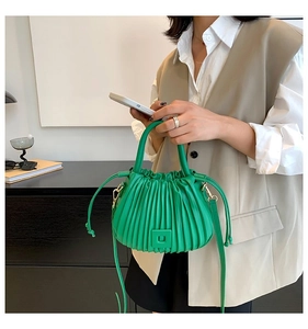 Detail showing bright green pleated bucket bag with fixed handle and adjustable strap