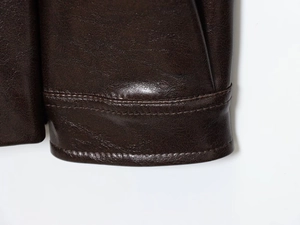 Detailed close-up of dark brown leather coat cuff showing premium texture and stitching