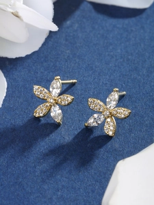 Macro shot of gold floral earrings with marquise-cut zircons on a dark blue background