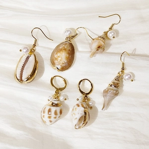 Detailed view of gold sea shell earrings and white pearls on white silk fabric