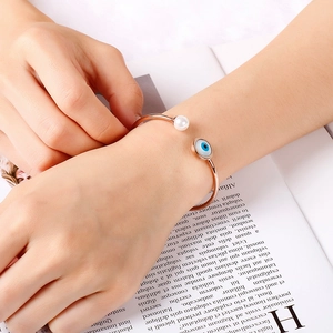 Close-up of rose gold bangle with pearl and blue evil eye charm on a magazine