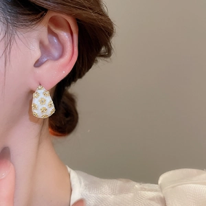 Close-up of vintage French earrings with golden flower accents on creamy enamel surface