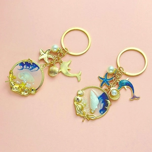 Detail of blue ocean resin charms with starfish, dolphin and sea shells on golden keychain