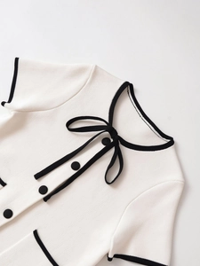 Detail of white knit short sleeve top with black contrast trim and bow necktie