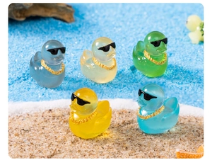 Miniature luminous resin ducks with sunglasses and gold chains on a sandy beach setting