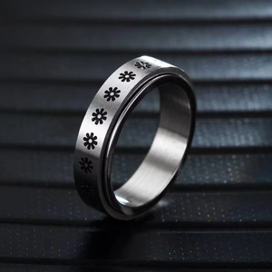Macro detail of stainless steel spinner ring with engraved black daisy flower patterns