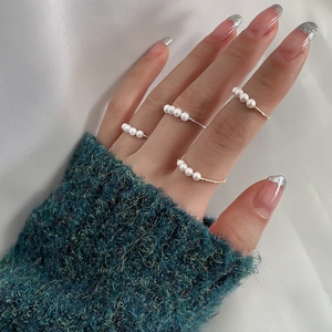 Detail showing four delicate gold and silver rings with pearls worn on a hand