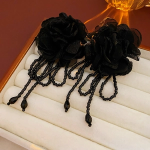 Close-up of elegant black fabric flower earrings with long beaded tassels in a white gift box