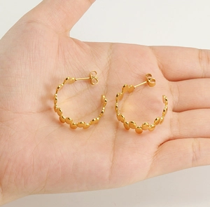 Detailed view of irregular textured 18k gold earrings held in hand for size reference