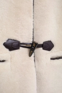 Détail du manteau en fausse fourrure crème avec boutons brandebourg marron foncé et cuir