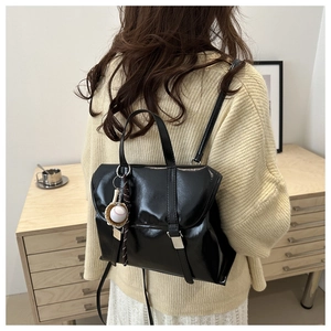 Détail d'un sac à dos en cuir verni noir avec breloques baseball et boucle en métal
