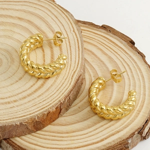 Detailed view of 18k gold plated twisted braided hoop earrings on a rustic wood slice
