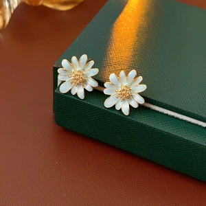 Detailansicht der weißen Gänseblümchen-Ohrringe auf einer grünen Geschenkbox mit Textur