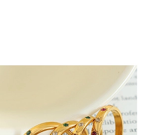 Macro detail of intertwined gold ring set with red green and white round gemstones