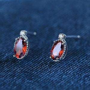 Macro shot of oval red gemstone stud earrings with silver prongs on blue fabric