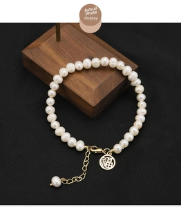Detail of natural pearl bracelet with golden Fu character pendant and lobster clasp