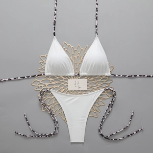 Flat lay of white bikini set with pink leopard print side ties on a grey textured surface